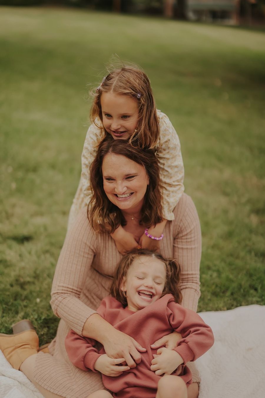 A mother laughing on the grass with her two children
