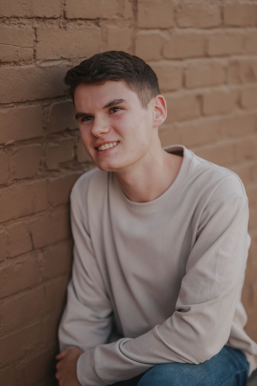 A high school senior smiling against a warm brick wall downtown