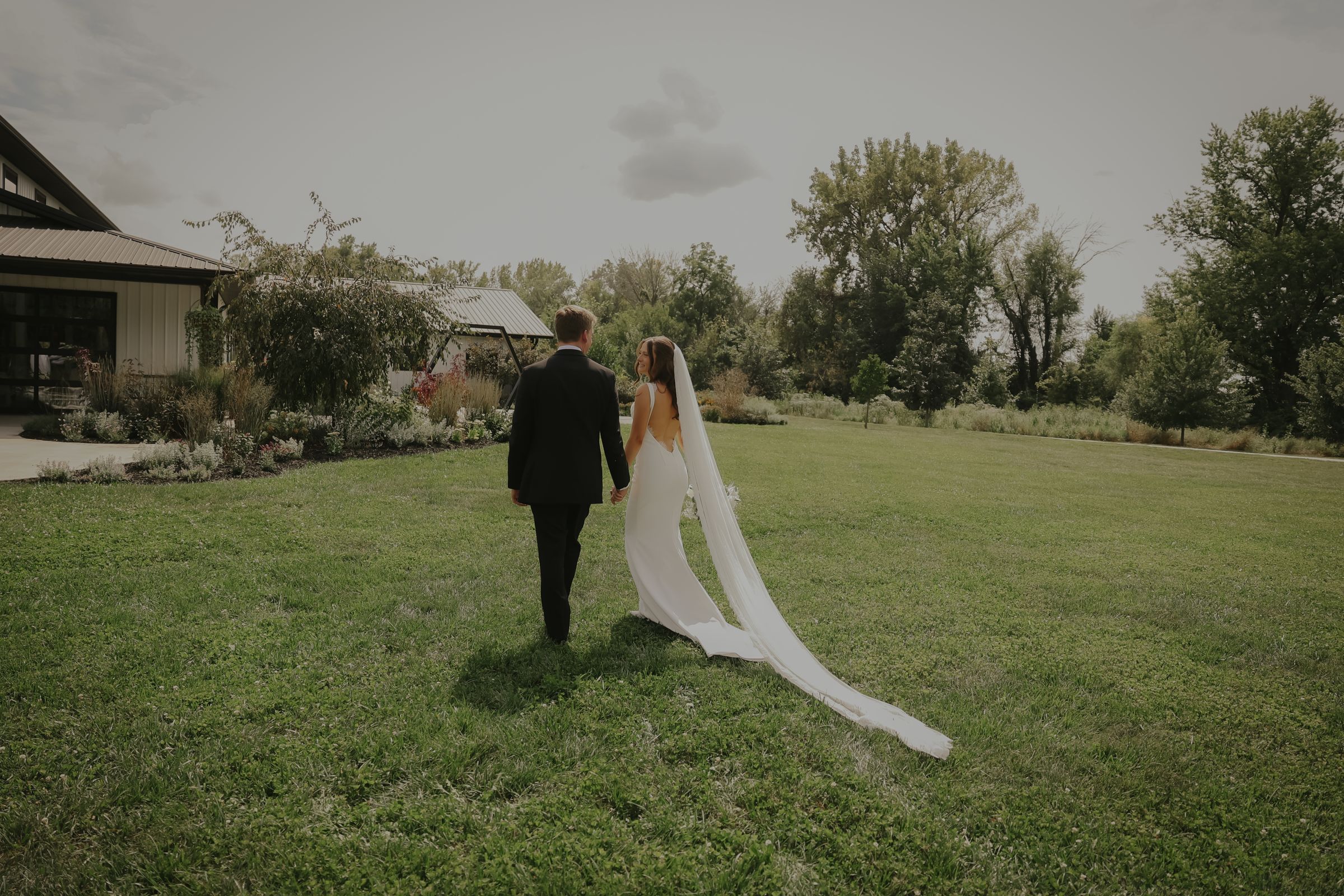A bride and groom walking away across an open lawn