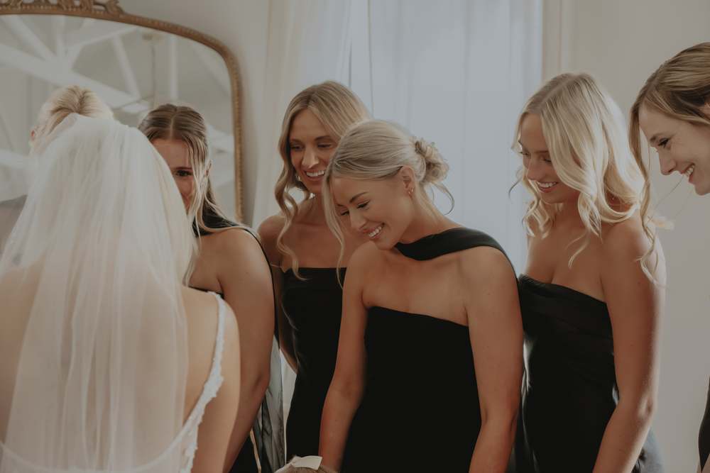 Bridesmaids laughing with the bride in the window light