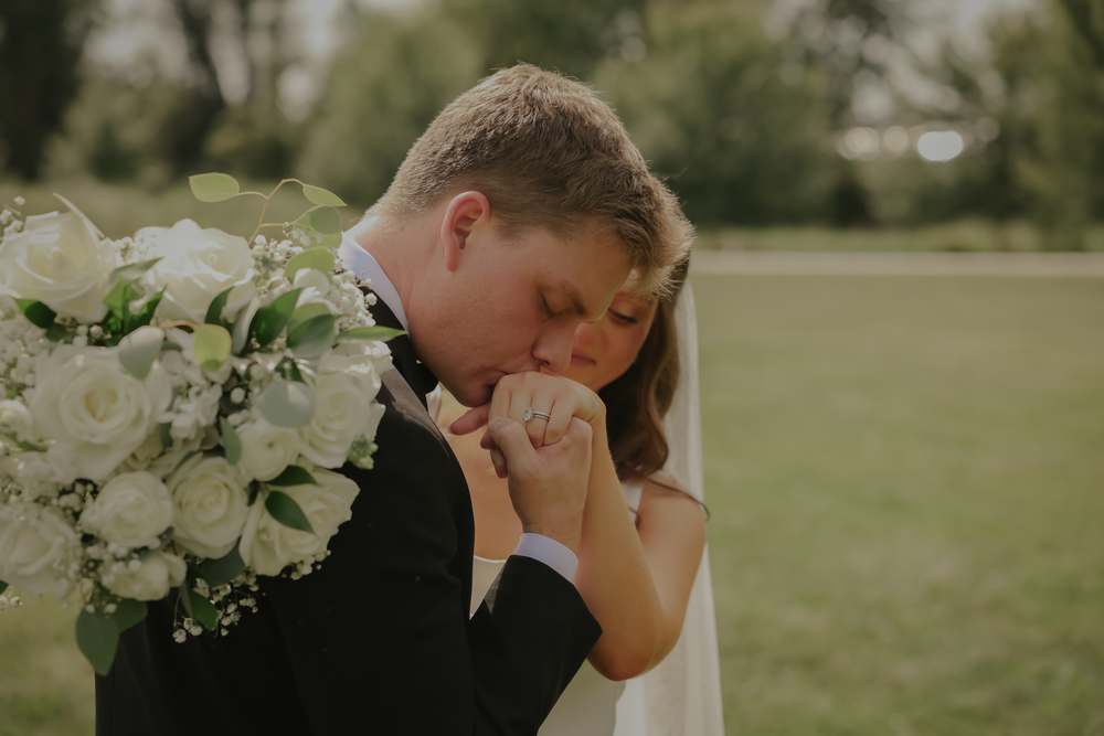 The groom kissing her hand behind the bouquet